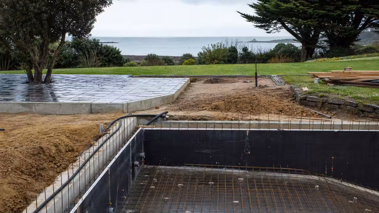 Chantier de piscine maçonnée avec ferraillage et terrasse en préparation dans un jardin breton