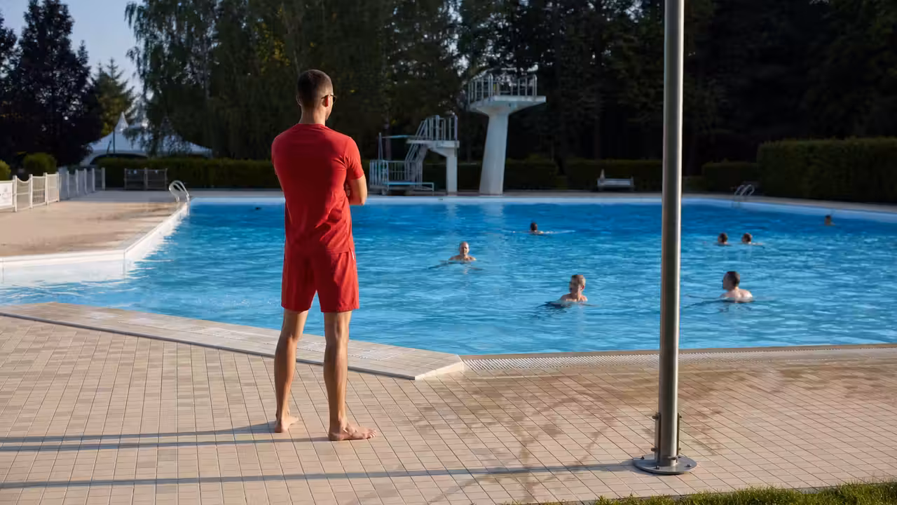 Bassin extérieur municipal surveillé, avec baigneurs espacés et maître-nageur en bord de plage