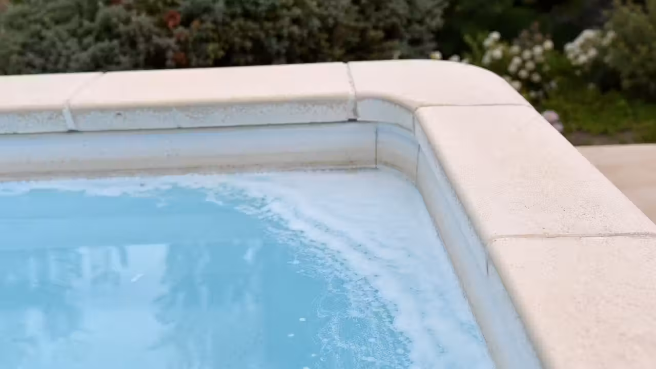 Écume blanche accumulée à la surface d'une piscine privée le long de la paroi, eau claire et margelles claires au soleil
