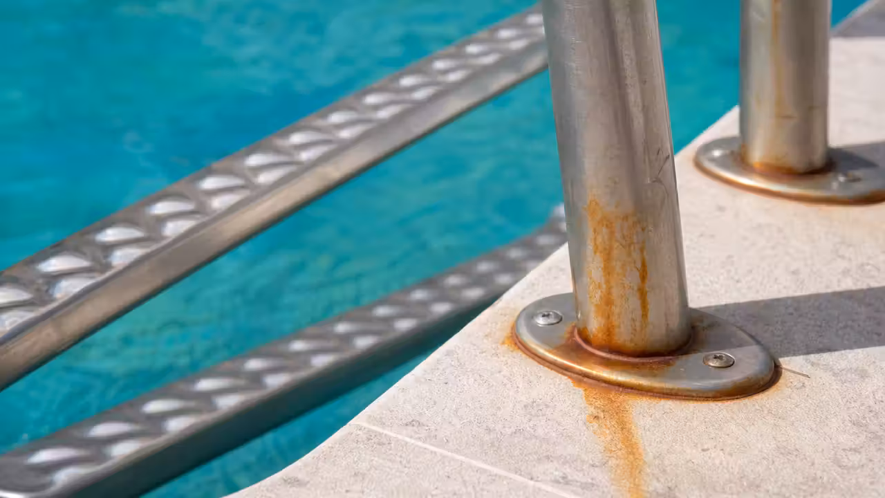Barreaux d'une échelle de piscine en inox présentant des traces de rouille orangée près des fixations