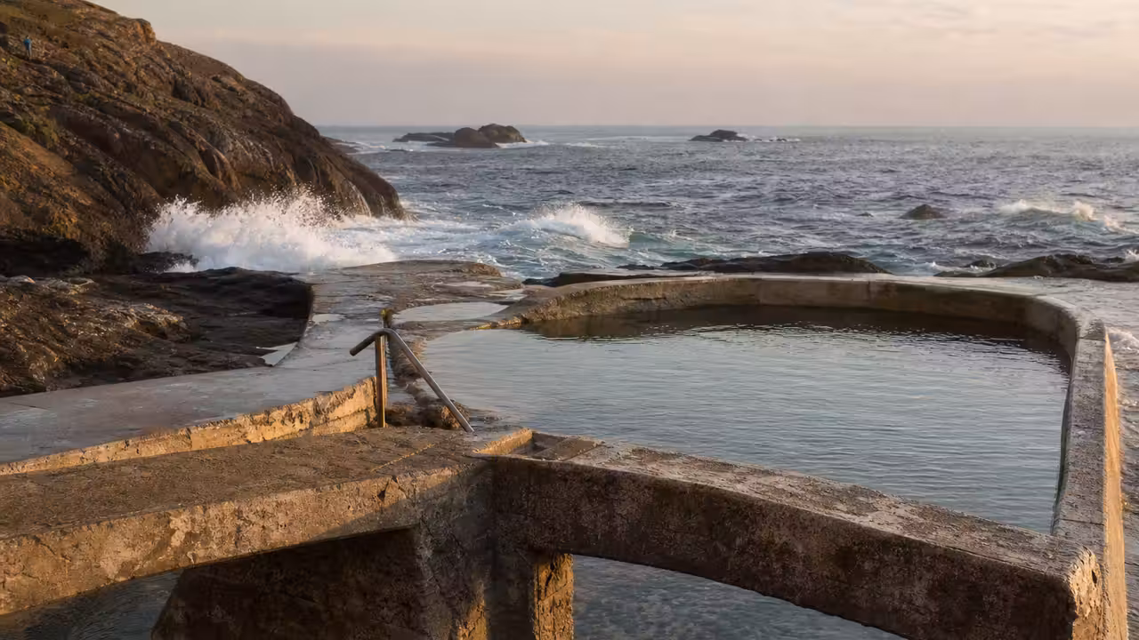 Bassin de mer en béton intégré aux rochers, ouvert sur l’océan sous une lumière matinale douce