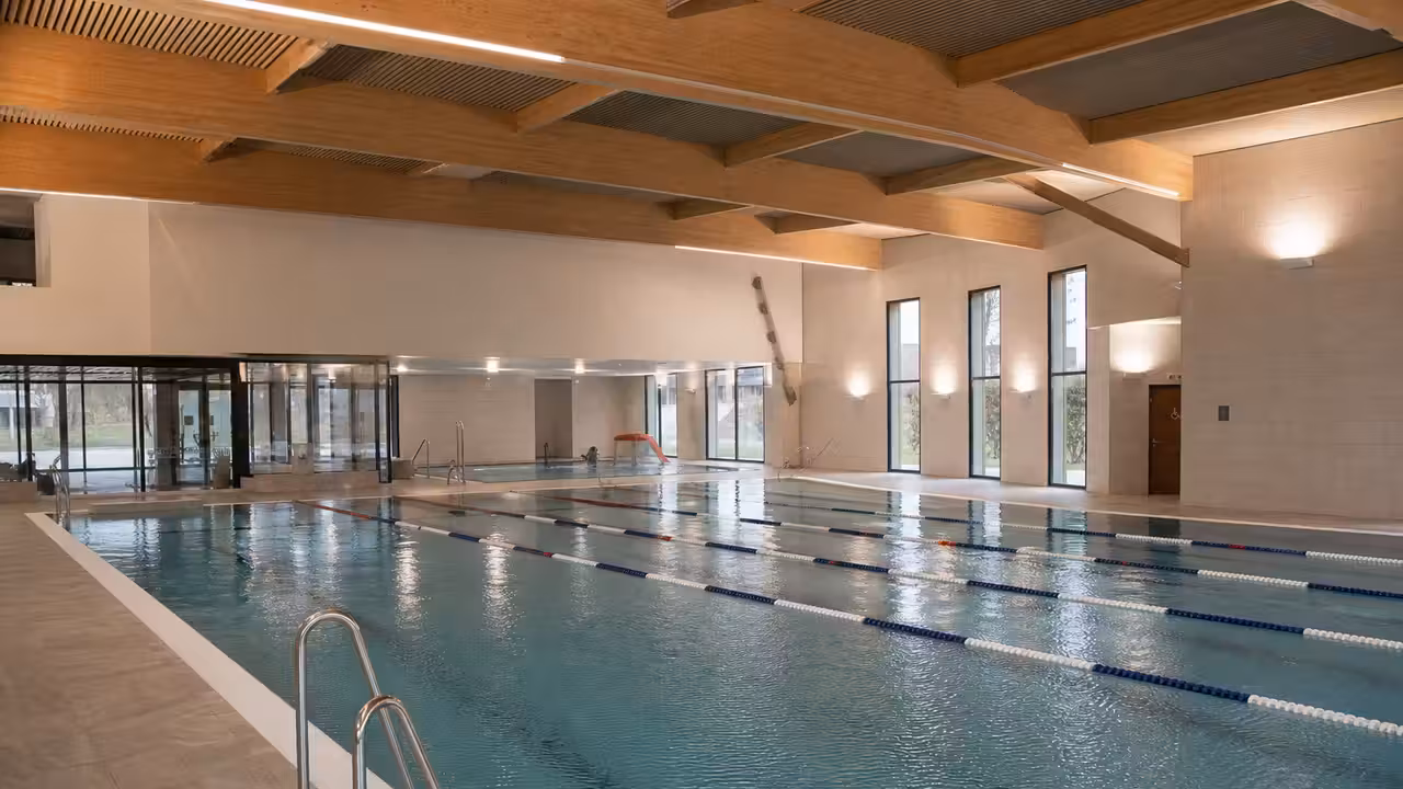 Vue intérieure d’une piscine publique rénovée avec bassin de nage, baies vitrées et vestiaires modernes