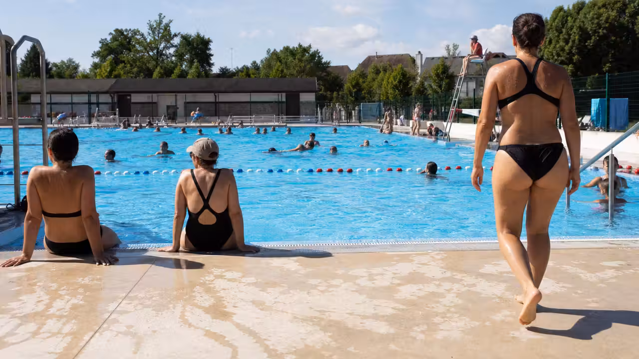 Bassin extérieur d’une piscine municipale animé lors d’une journée d’été, avec surveillant en arrière-plan