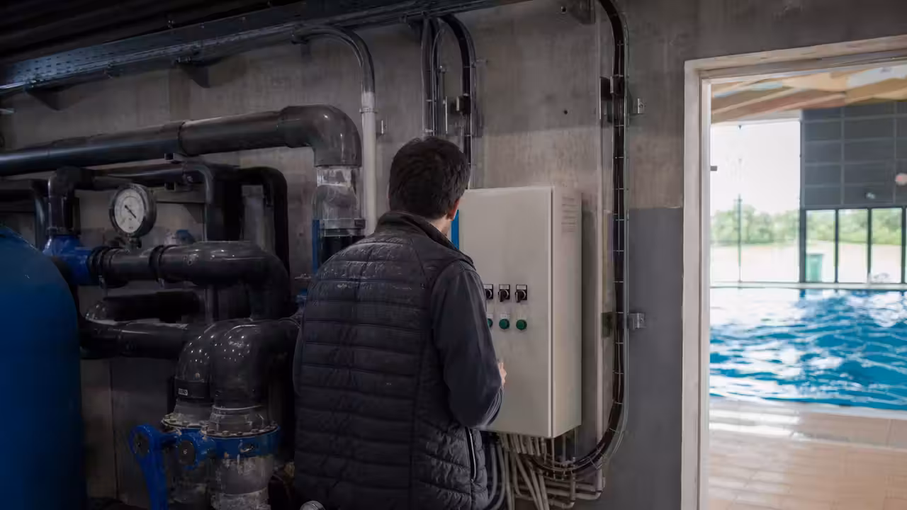 Technicien examinant les pompes et filtres dans le local technique d’une piscine municipale rénovée