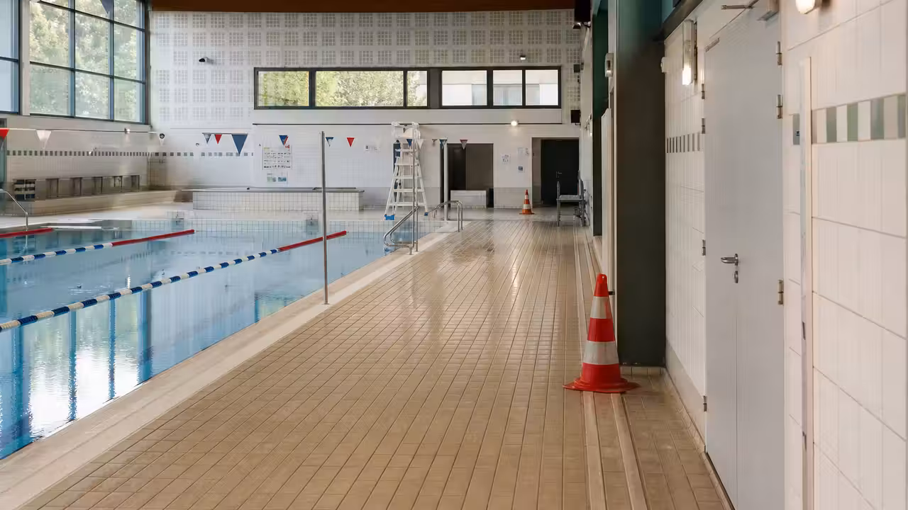 Bassin couvert municipal vide après évacuation, avec accès au local technique sécurisé en arrière-plan