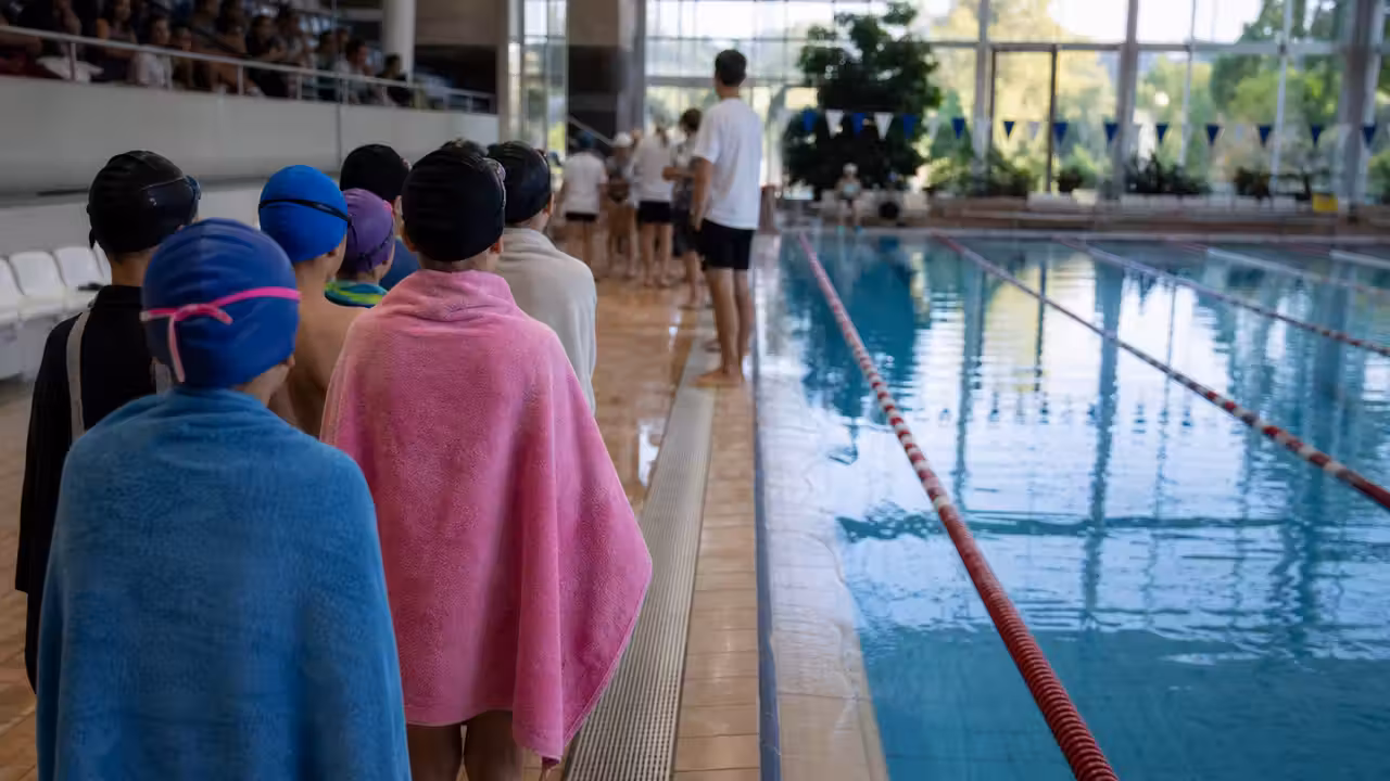 Jeunes nageurs vus de dos au bord d’un bassin couvert avant une session encadrée