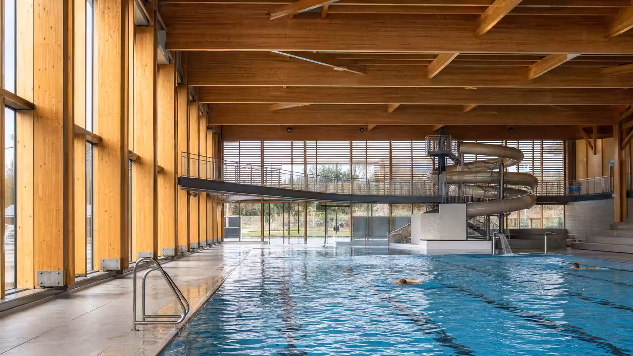 Bassin intérieur lumineux d’un centre aquatique moderne avec façade et détails de structure en bois