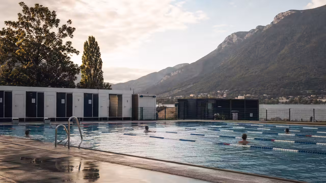 Bassin municipal extérieur temporaire avec lignes d’eau, vestiaires modulaires et reliefs alpins en arrière-plan