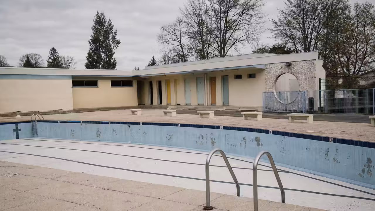 Bassin municipal extérieur vide, avec lignes d’eau retirées et bâtiment technique vieillissant en arrière-plan