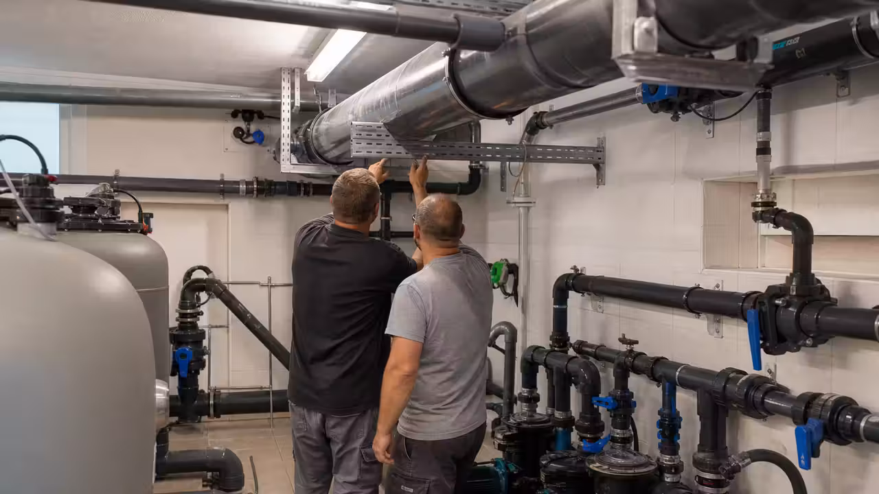 Local technique d’une piscine publique avec canalisations, pompes et vannes en cours d’inspection