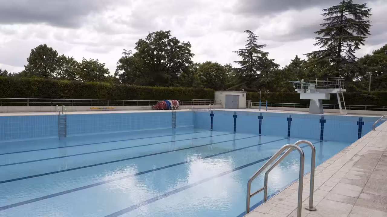 Bassin municipal vide avec lignes d’eau, gradins et équipements techniques en arrière-plan