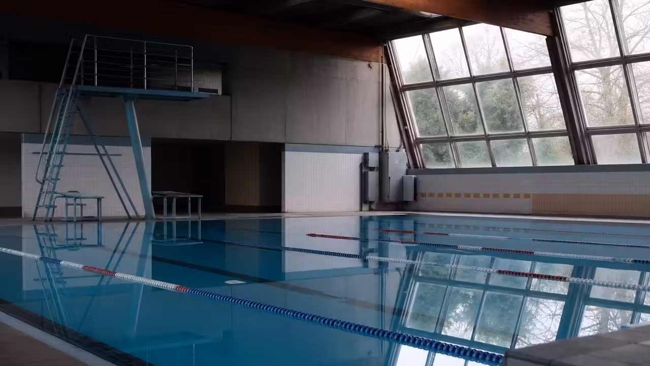 Bassin couvert municipal vide avec lignes d’eau et éclairage éteint pendant une fermeture technique