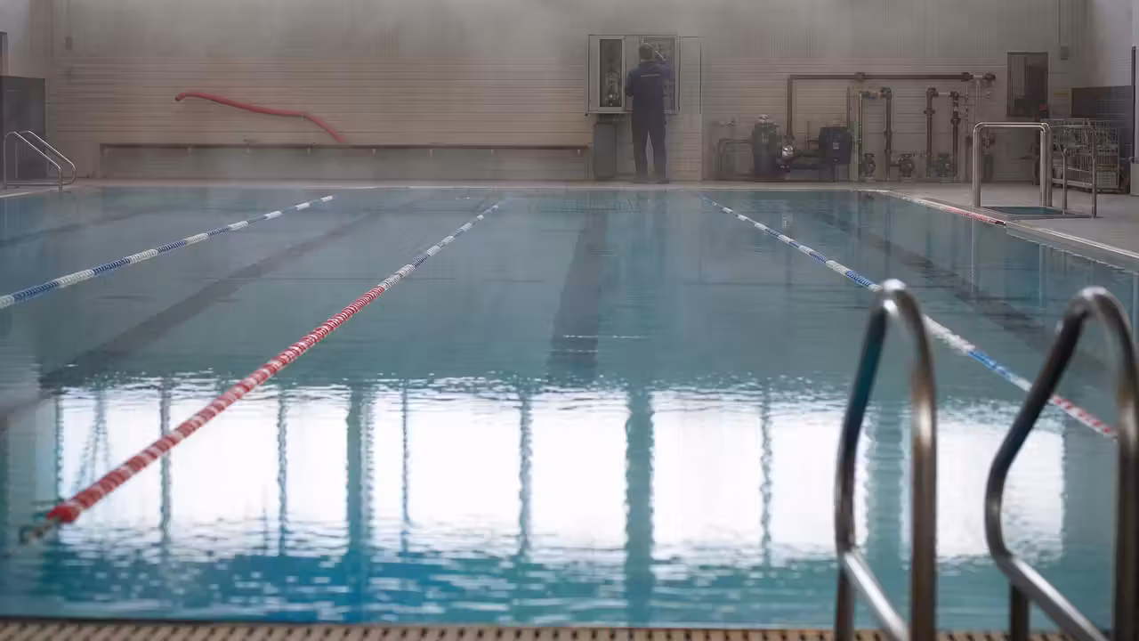 Bassin intérieur vide avec lignes d’eau et technicien contrôlant la régulation thermique en arrière-plan
