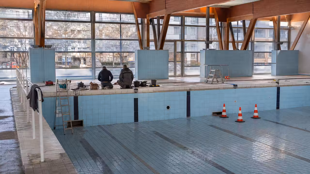 Bassin sportif vide en rénovation avec parois carrelées, échafaudage léger et matériel de maintenance