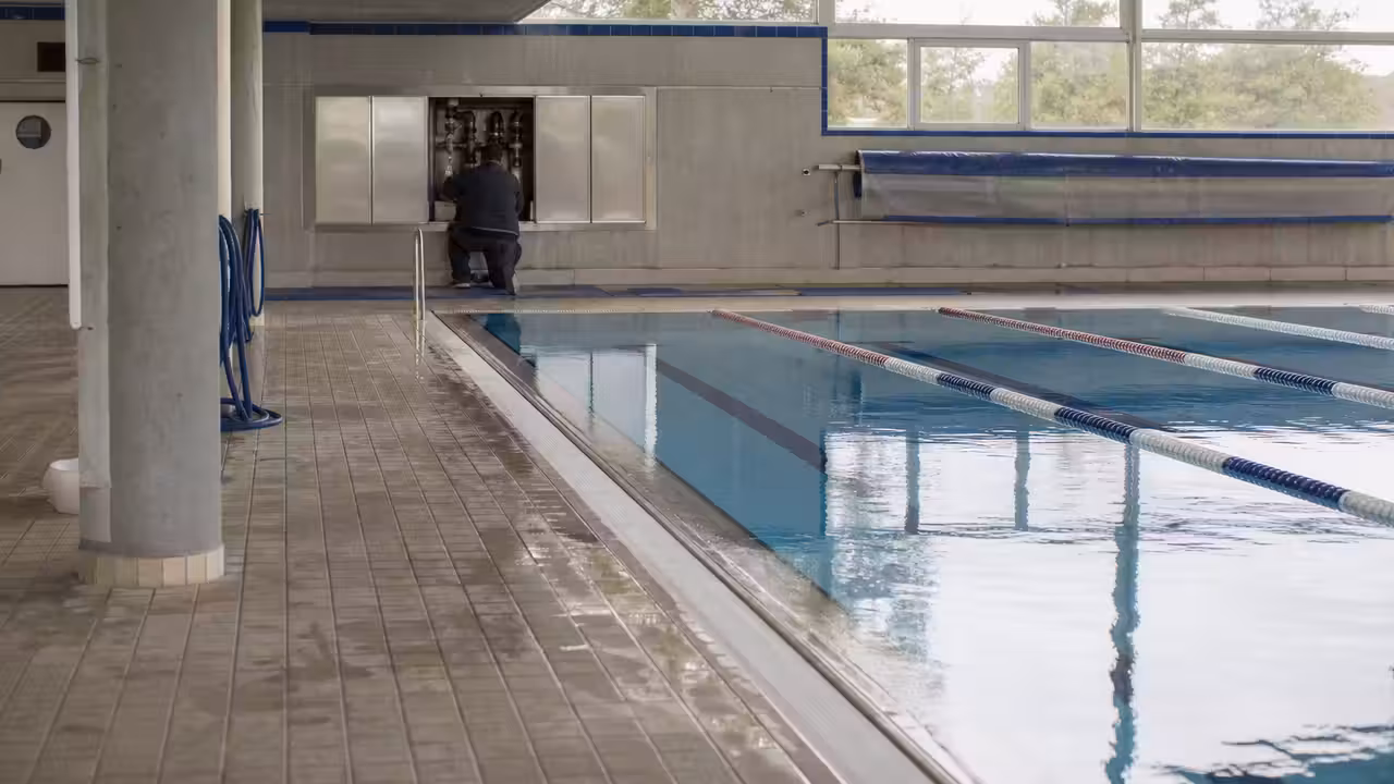 Bassin couvert vide d'une piscine municipale, avec lignes d'eau et équipements techniques en maintenance