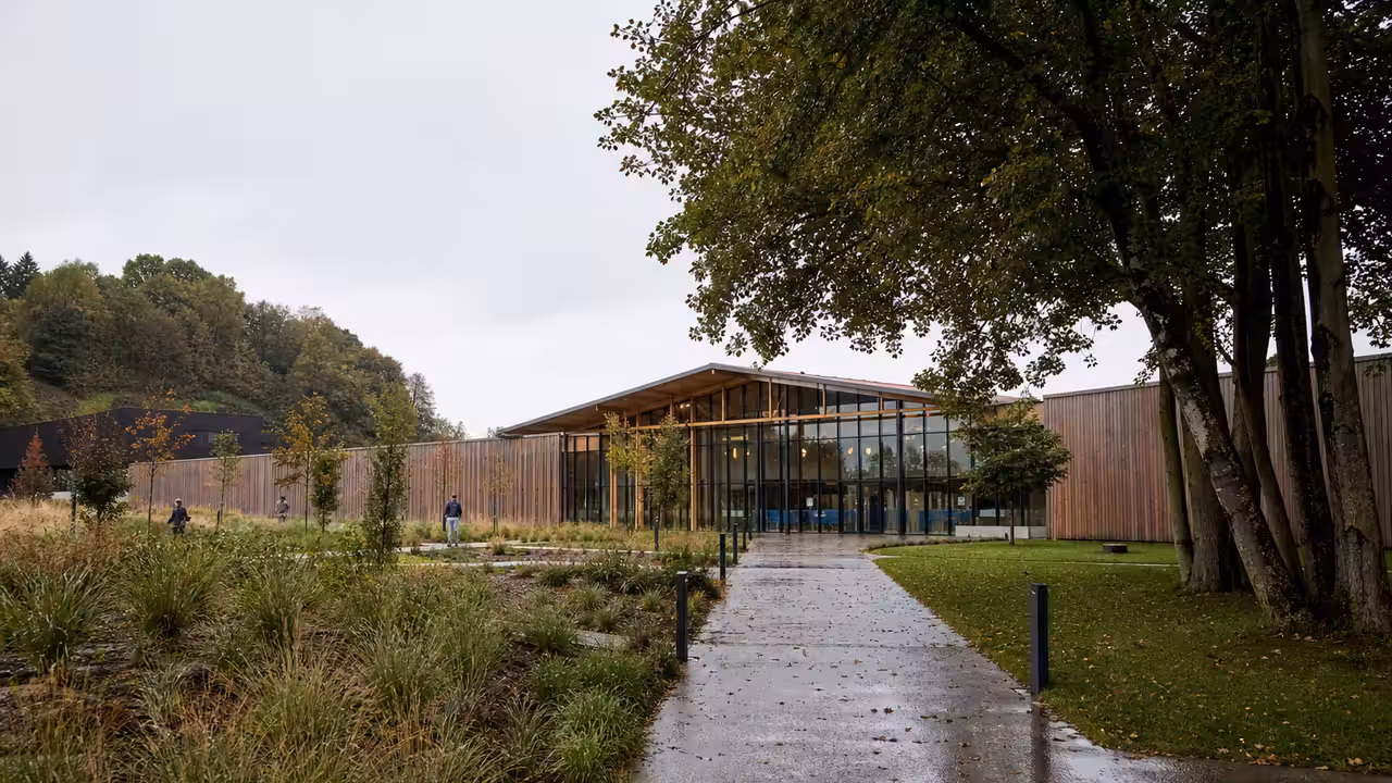 Vue extérieure d’un centre aquatique public contemporain en bois, intégré à un paysage verdoyant basque.