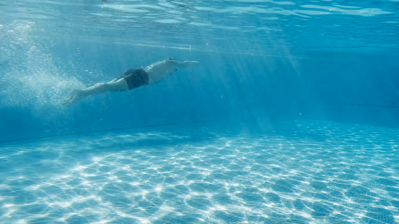 Nageur en apnée sous l'eau d'une piscine, vu de profil, silhouette immergée dans une eau turquoise claire