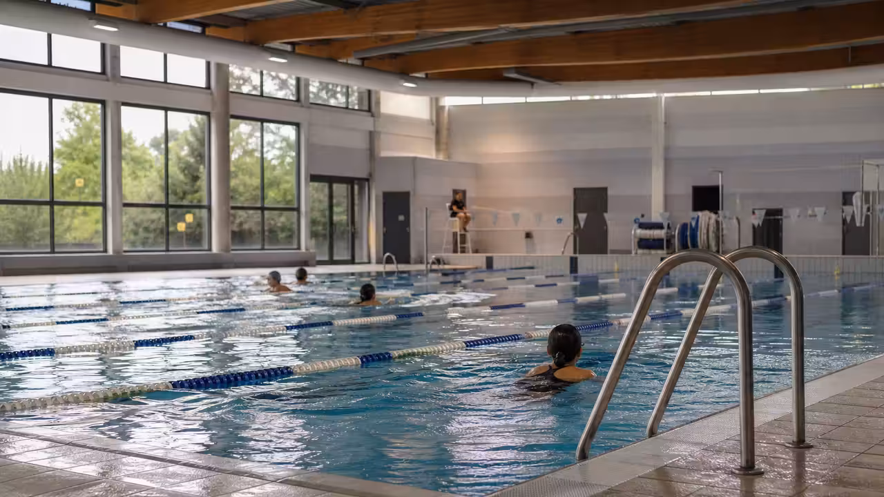 Nageurs dans les lignes d’eau d’une piscine municipale rénovée et lumineuse, vue d’ensemble