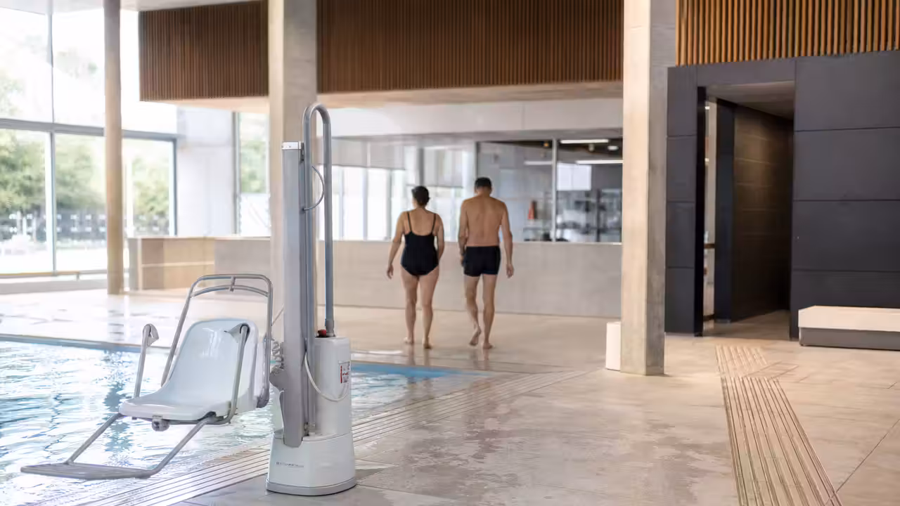 Accès de piscine publique moderne avec rampe, signalétique tactile et appareil de mise à l’eau au bord du bassin