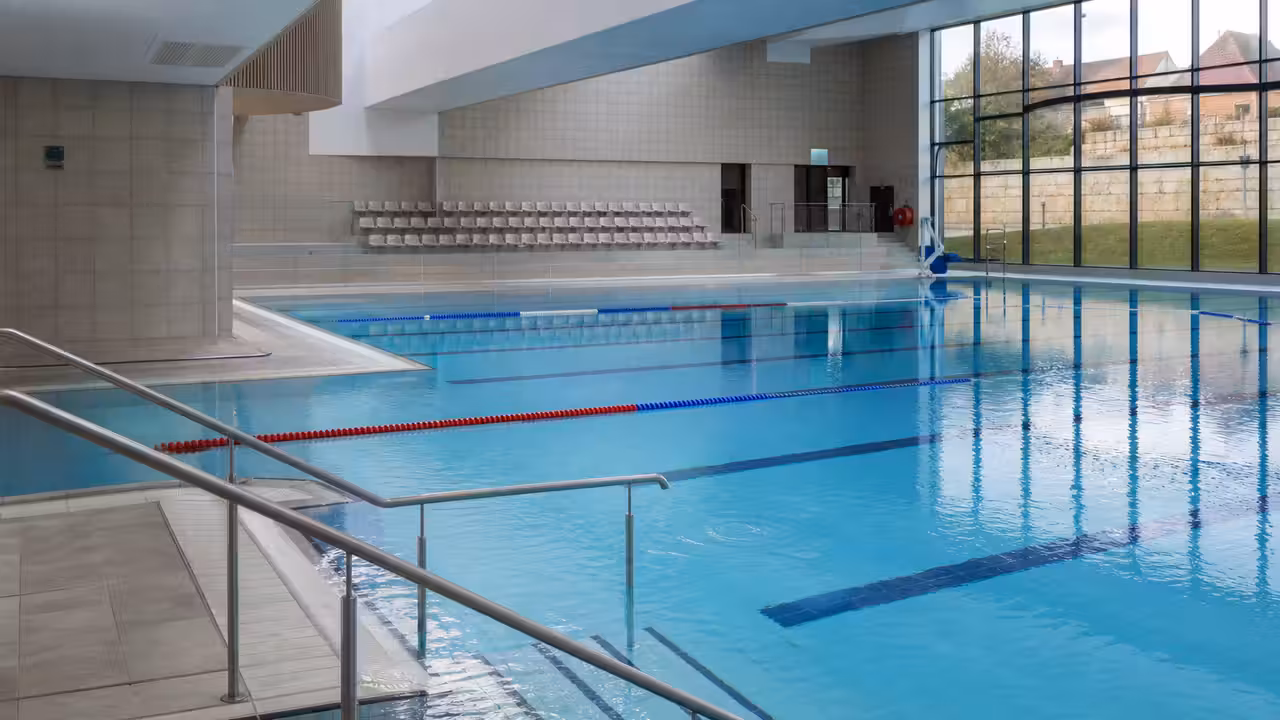 Bassin municipal moderne avec lignes de nage, vestiaires vitrés et accès de plain-pied pour les usagers