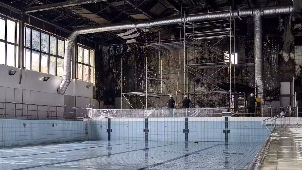Bassin municipal vide en rénovation, avec échafaudages et équipements techniques dans une piscine couverte