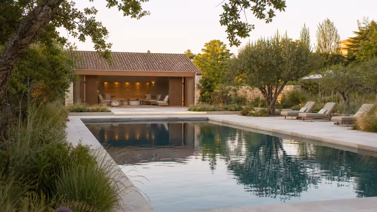 Piscine extérieure contemporaine entourée de pierre naturelle, terrasse paysagée et pool house en bois
