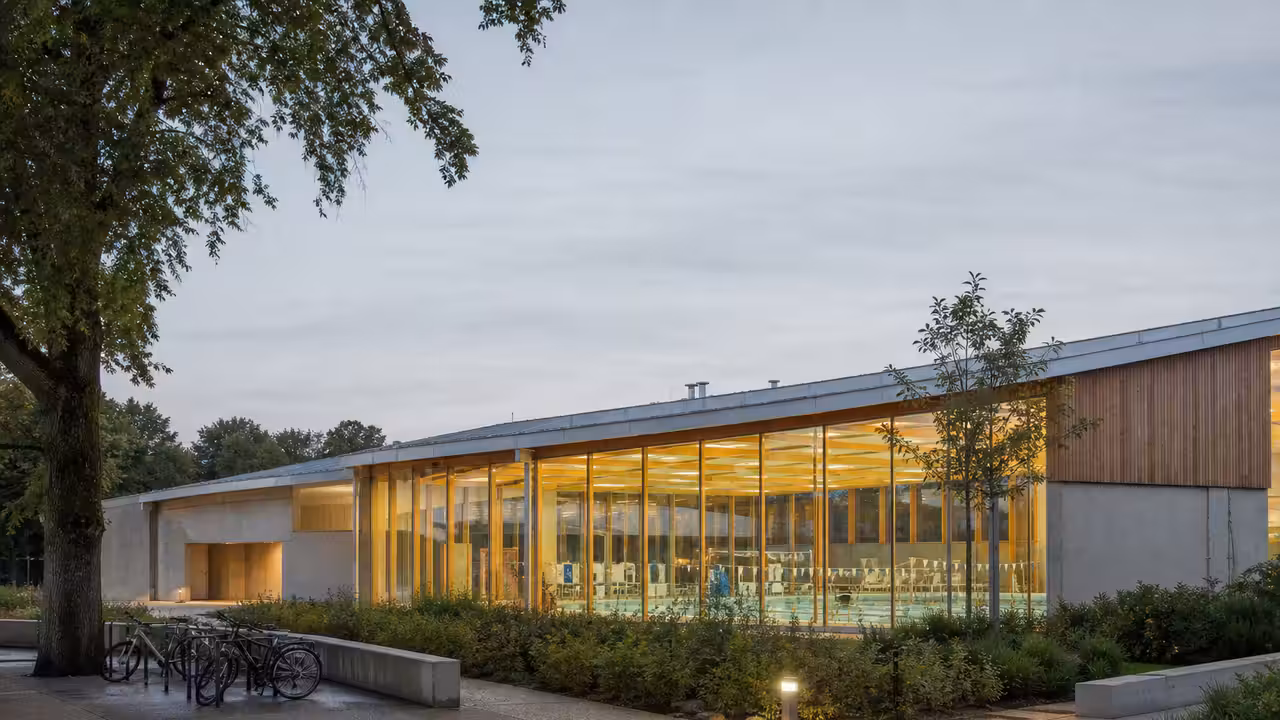 Façade vitrée d’un centre aquatique public contemporain, bordée d’arbres et de cheminements piétons