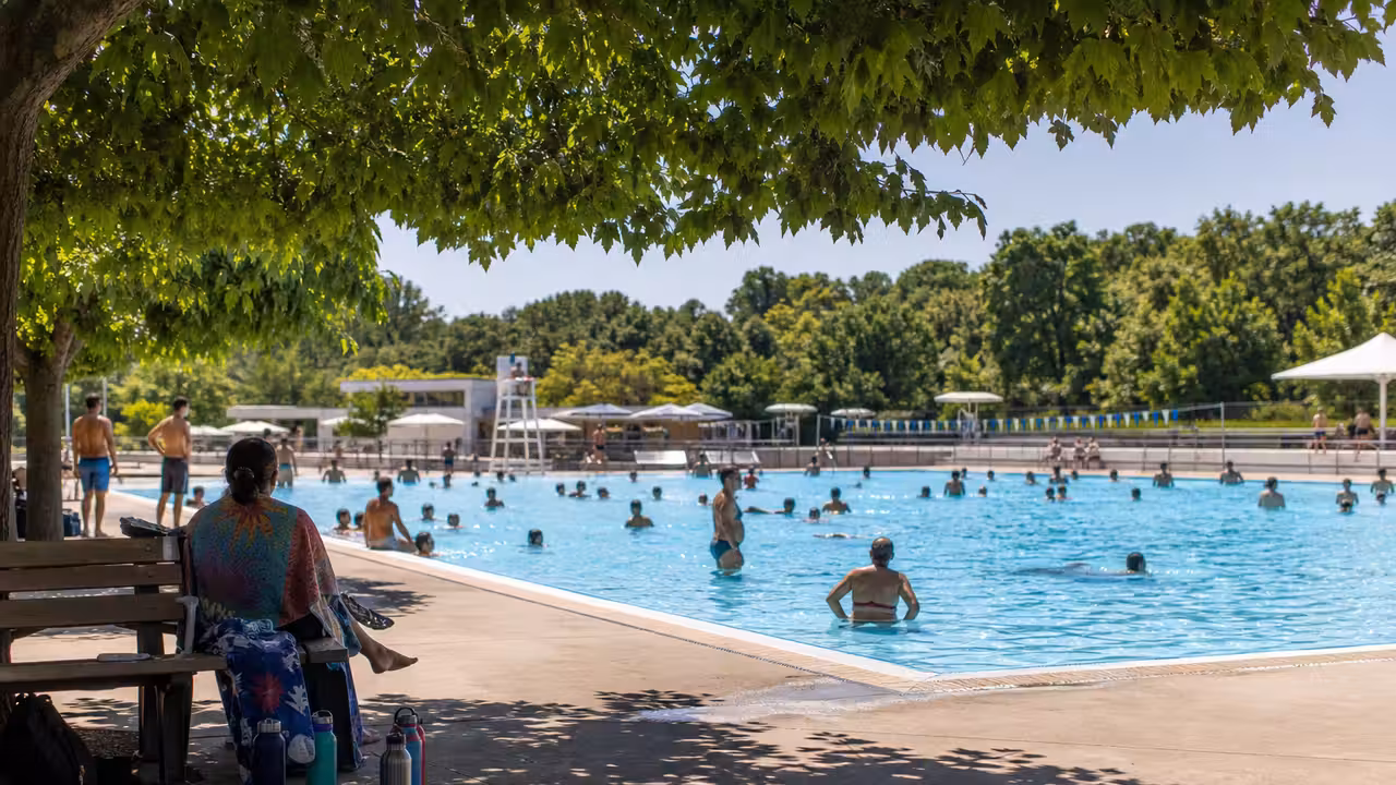 Bassin municipal extérieur fréquenté pendant une journée de forte chaleur, avec zones d’ombre autour de l’eau
