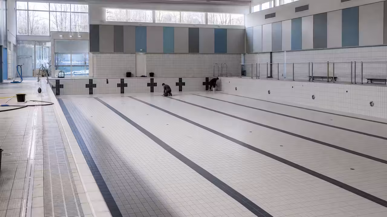 Bassin sportif couvert vidé pour entretien, avec carrelage et équipements techniques visibles au fond