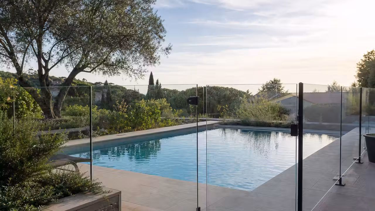 Barrière de sécurité vitrée et portillon fermé autour d’une piscine privée contemporaine en terrasse.