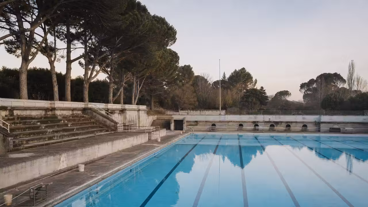 Ancien bassin municipal extérieur aux lignes d’eau vides, évoquant l’histoire des piscines publiques des années 1960