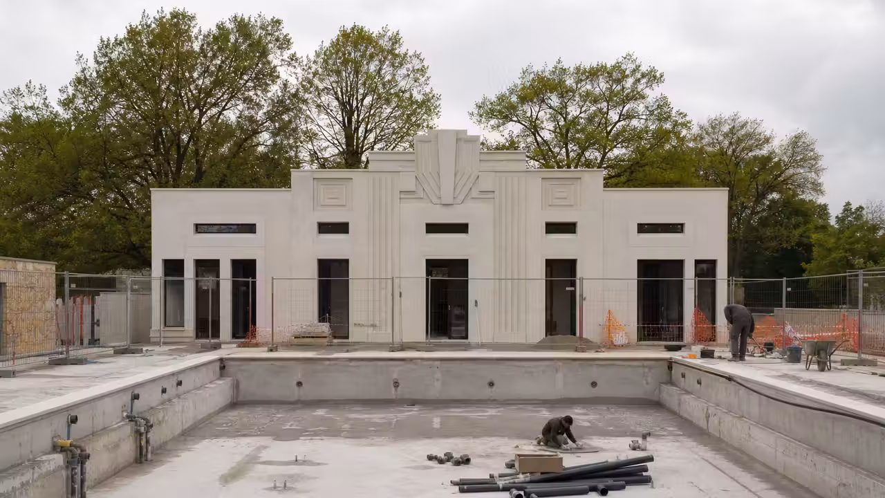 Bassin extérieur historique en rénovation avec plages claires, vestiaires et structures Art déco en arrière-plan