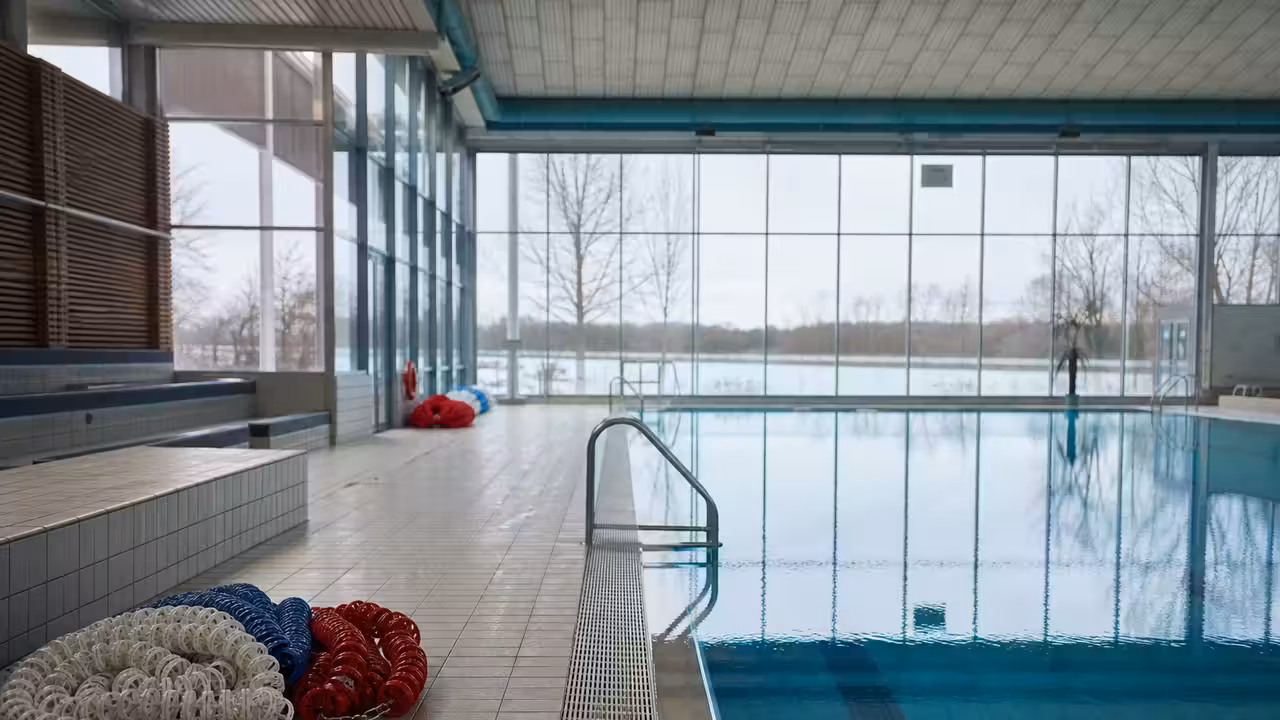 Bassin couvert municipal vide en hiver, avec lignes d’eau et baies vitrées donnant sur un paysage froid