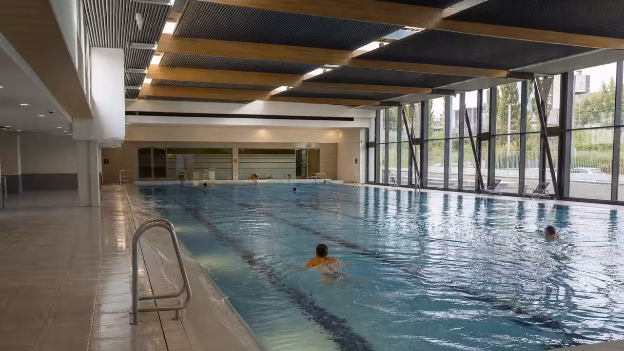 Bassin de 25 mètres rénové d’une piscine publique, avec baies vitrées et lignes de nage vides
