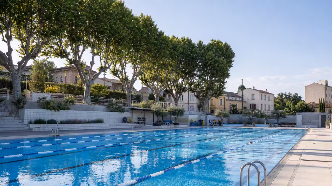 Bassin extérieur municipal en été avec lignes d’eau, plages minérales et végétation méditerranéenne