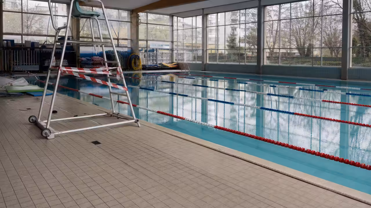 Bassin intérieur de piscine municipale vide, lignes d’eau calmes et poste de surveillance inoccupé