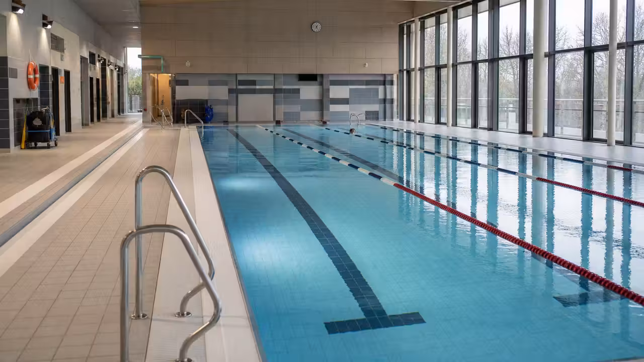 Bassin intérieur d’une piscine municipale rénovée, avec lignes d’eau, baies vitrées et vestiaires lumineux en arrière-plan
