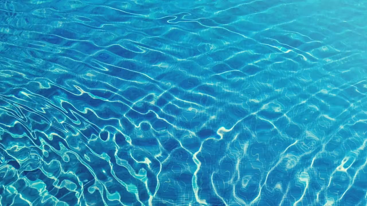 Bassin extérieur d’une piscine publique avec nageurs éloignés et maître-nageur surveillant depuis le bord