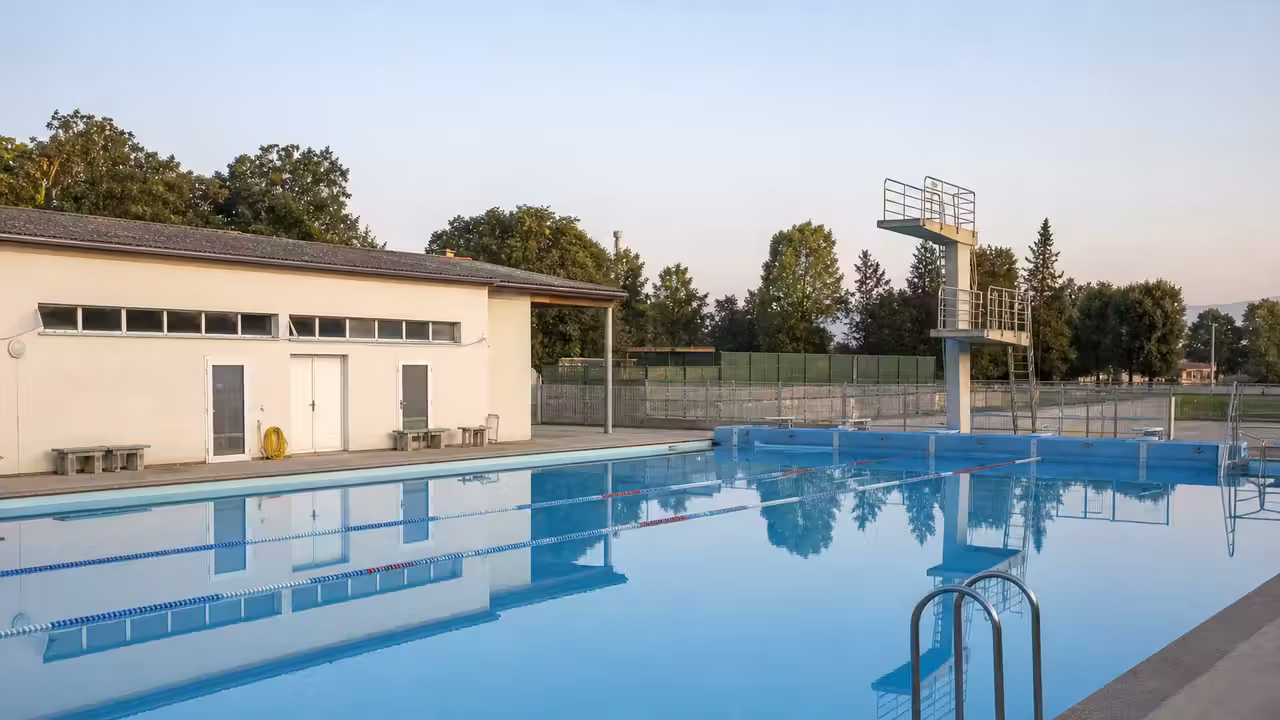 Bassin extérieur d’une piscine municipale française, bâtiments techniques et gradins vides en lumière matinale