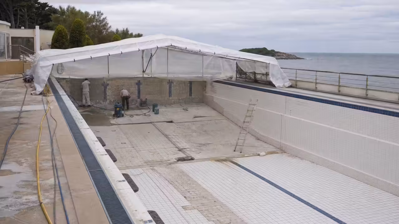 Bassin municipal vide en rénovation, protégé par une structure temporaire et entouré d’équipements de chantier