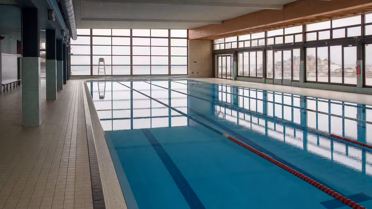 Bassin intérieur d’une piscine publique avec lignes d’eau, gradins et lumière naturelle un dimanche matin