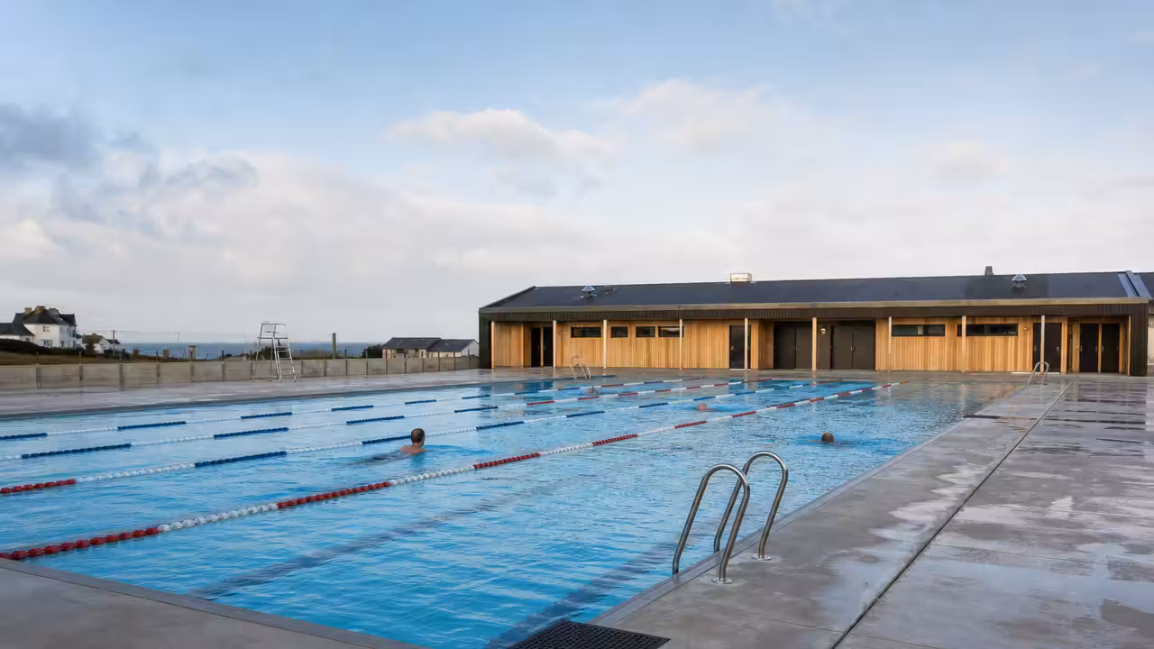 Bassin extérieur rénové d'une piscine publique, lignes d'eau tendues et plages humides au matin.