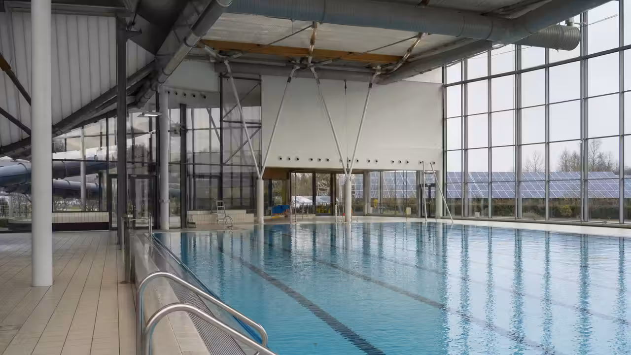 Bassin intérieur d’un centre aquatique municipal avec baies vitrées, lignes d’eau et équipements techniques discrets