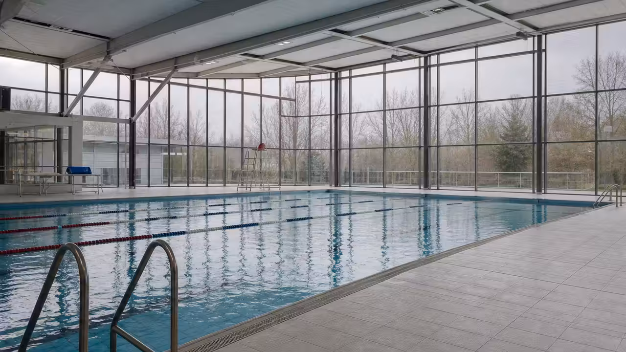 Nageurs dans un bassin couvert lumineux, avec lignes d’eau et maîtres-nageurs en surveillance au bord