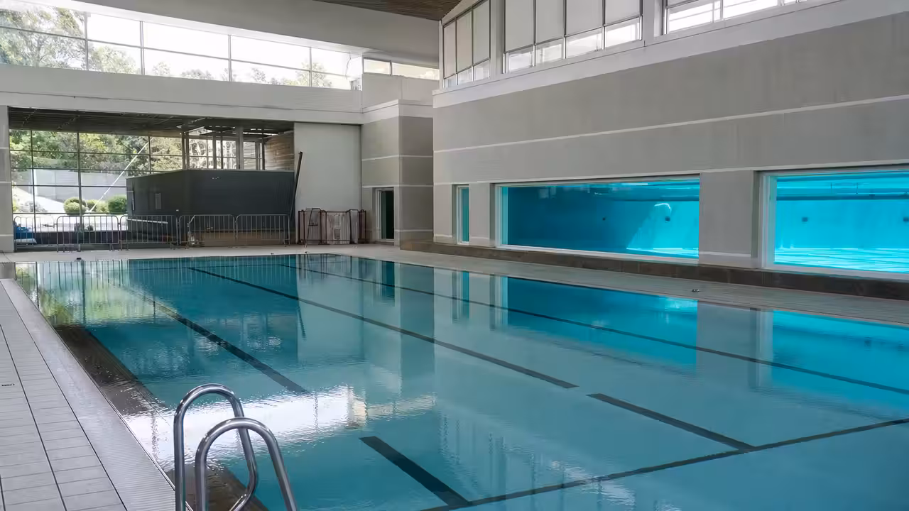 Vue intérieure d’un centre aquatique avec bassins vides et technicien contrôlant une paroi vitrée