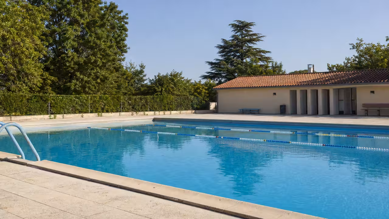 Bassin extérieur de piscine municipale entouré d’arbres, avec lignes d’eau et plage minérale vide
