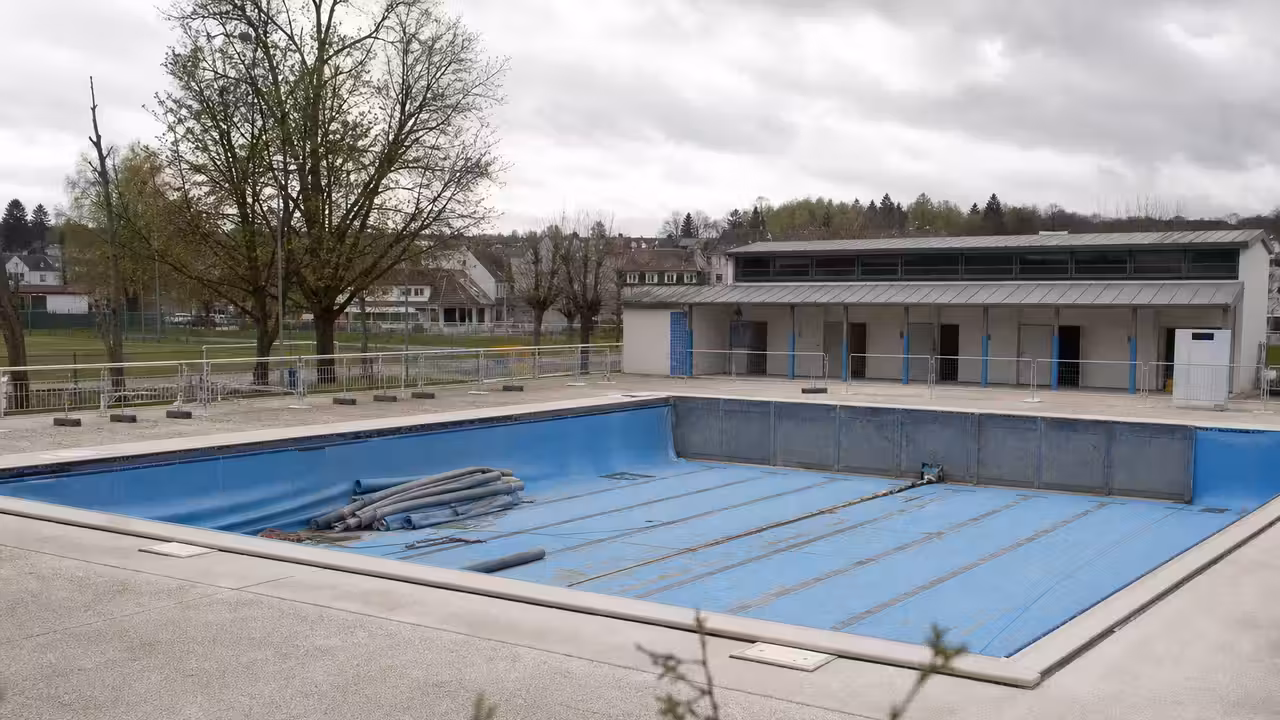 Bassin extérieur municipal vide en rénovation, avec plages minérales et équipements techniques en arrière-plan