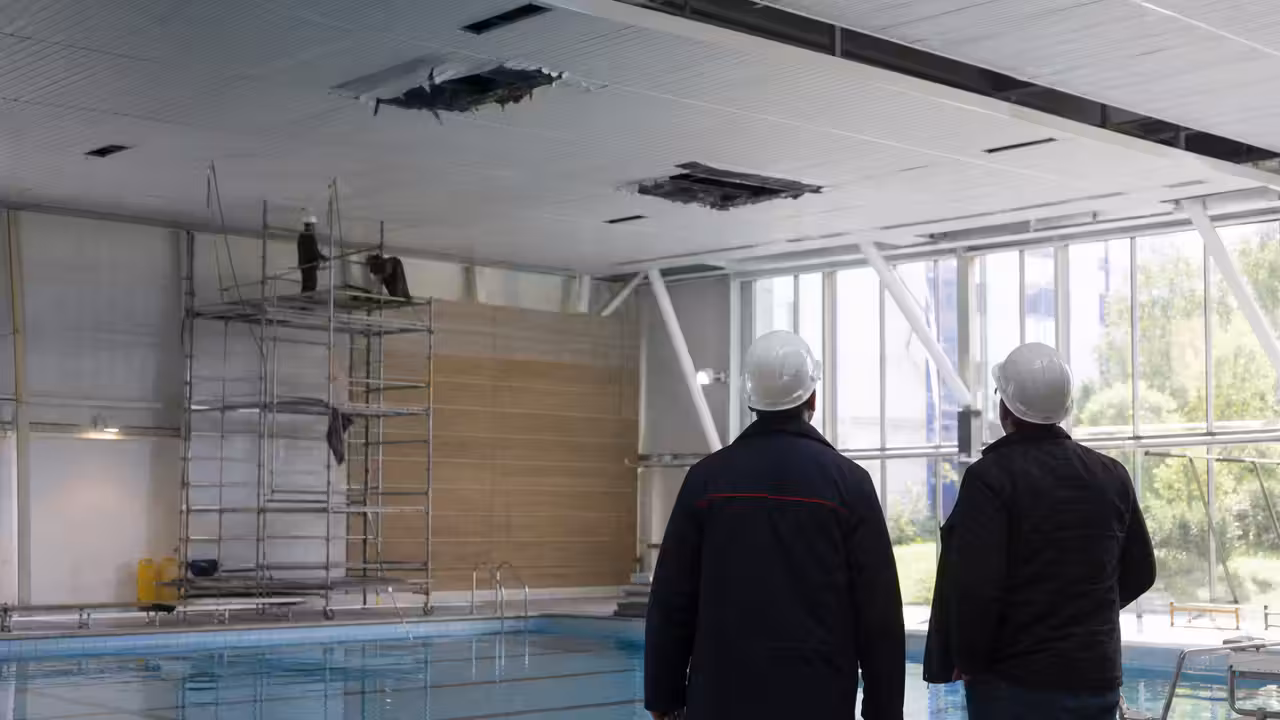 Toiture d’un centre aquatique municipal en cours d’inspection, avec échafaudage et bassin vide en arrière-plan