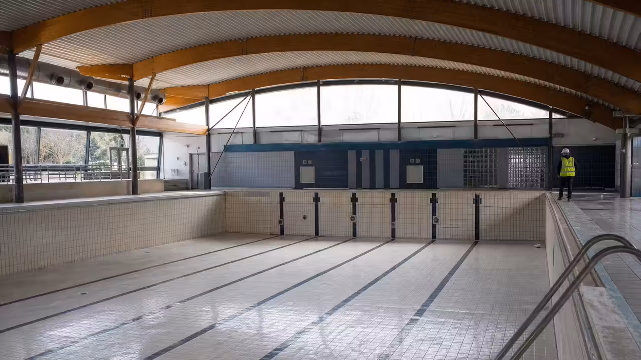 Bassin couvert municipal vide pendant une inspection technique, avec carrelage, lignes d’eau retirées et lumière naturelle
