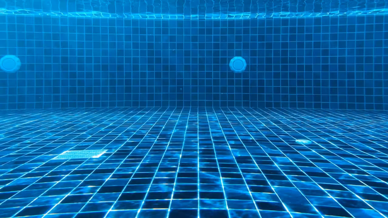 Bassin circulaire extérieur rénové, plages minérales et arbres autour d’une piscine publique estivale